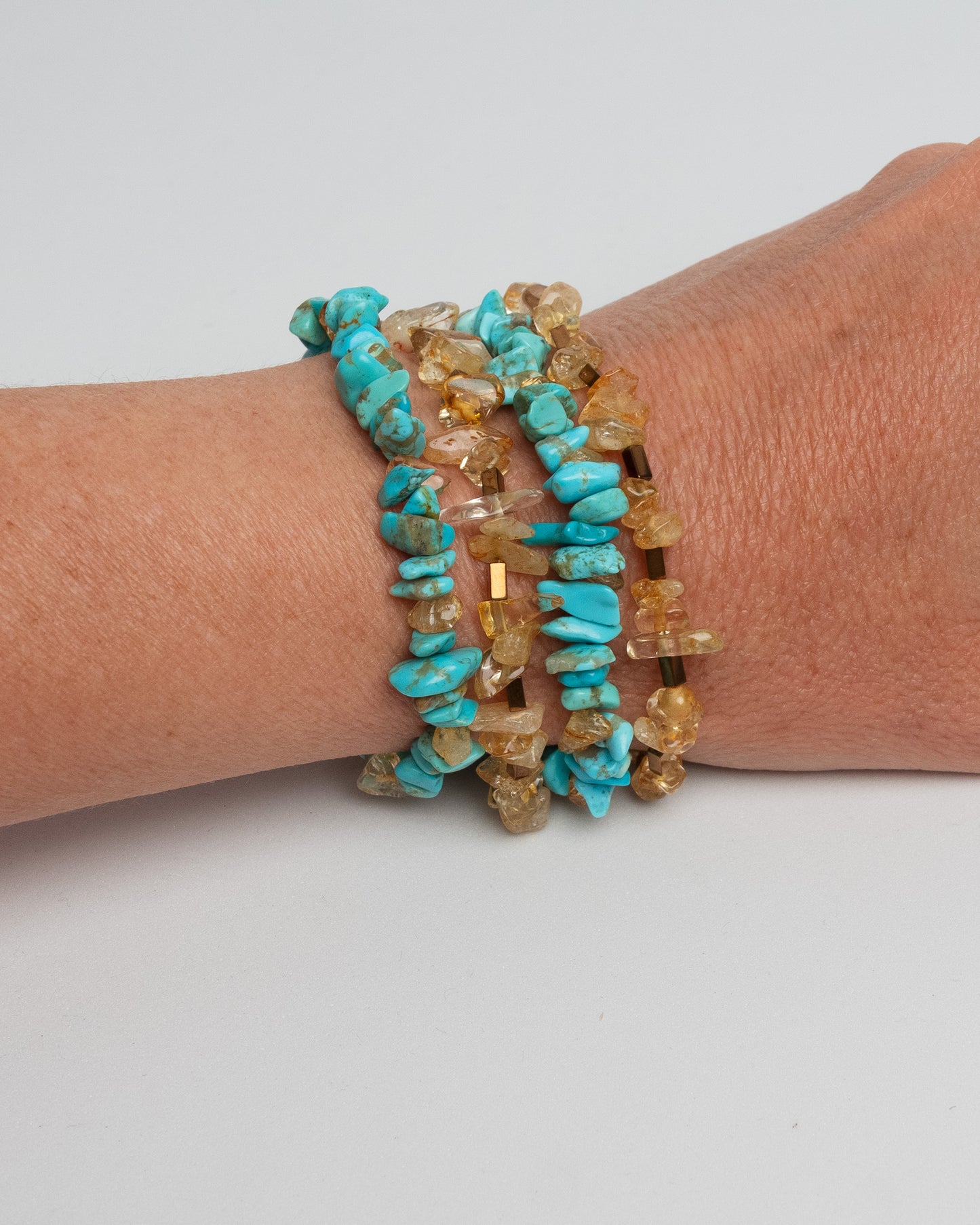 Layered gemstone bracelet for women featuring four chunky strands of natural turquoise, sunstone, and hematite beads. Multicolor summer statement bracelet with sterling silver T-bar clasp. Handmade multistrand accessory, bold and colorful jewelry inspired by Mediterranean style. One of a kind, artisanal, natural gemstone jewelry for a curated boho or elegant outfit.