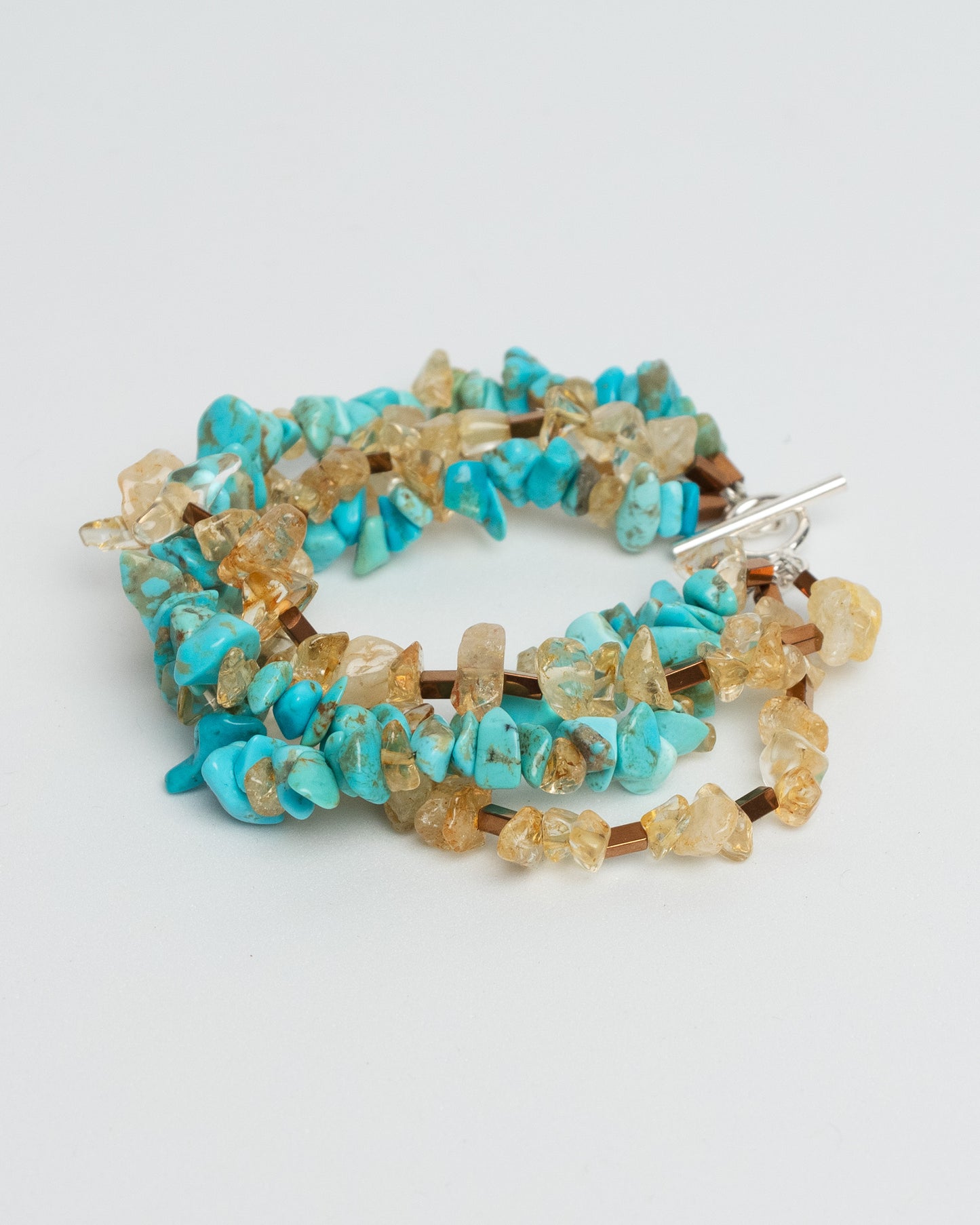 Layered gemstone bracelet for women featuring four chunky strands of natural turquoise, sunstone, and hematite beads. Multicolor summer statement bracelet with sterling silver T-bar clasp. Handmade multistrand accessory, bold and colorful jewelry inspired by Mediterranean style. One of a kind, artisanal, natural gemstone jewelry for a curated boho or elegant outfit.