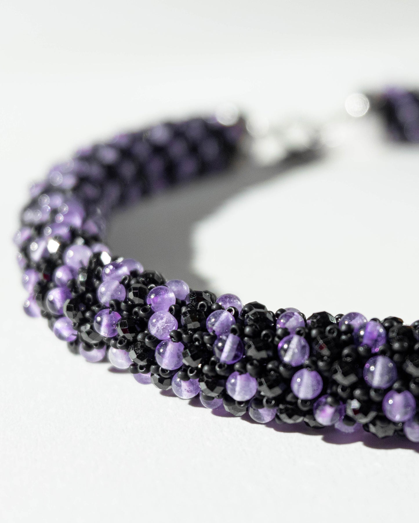 A luxurious amethyst and black spinel necklace with a silver T-bar clasp, featuring vibrant purple and dark sparkling gemstones, crafted in a collar-length design