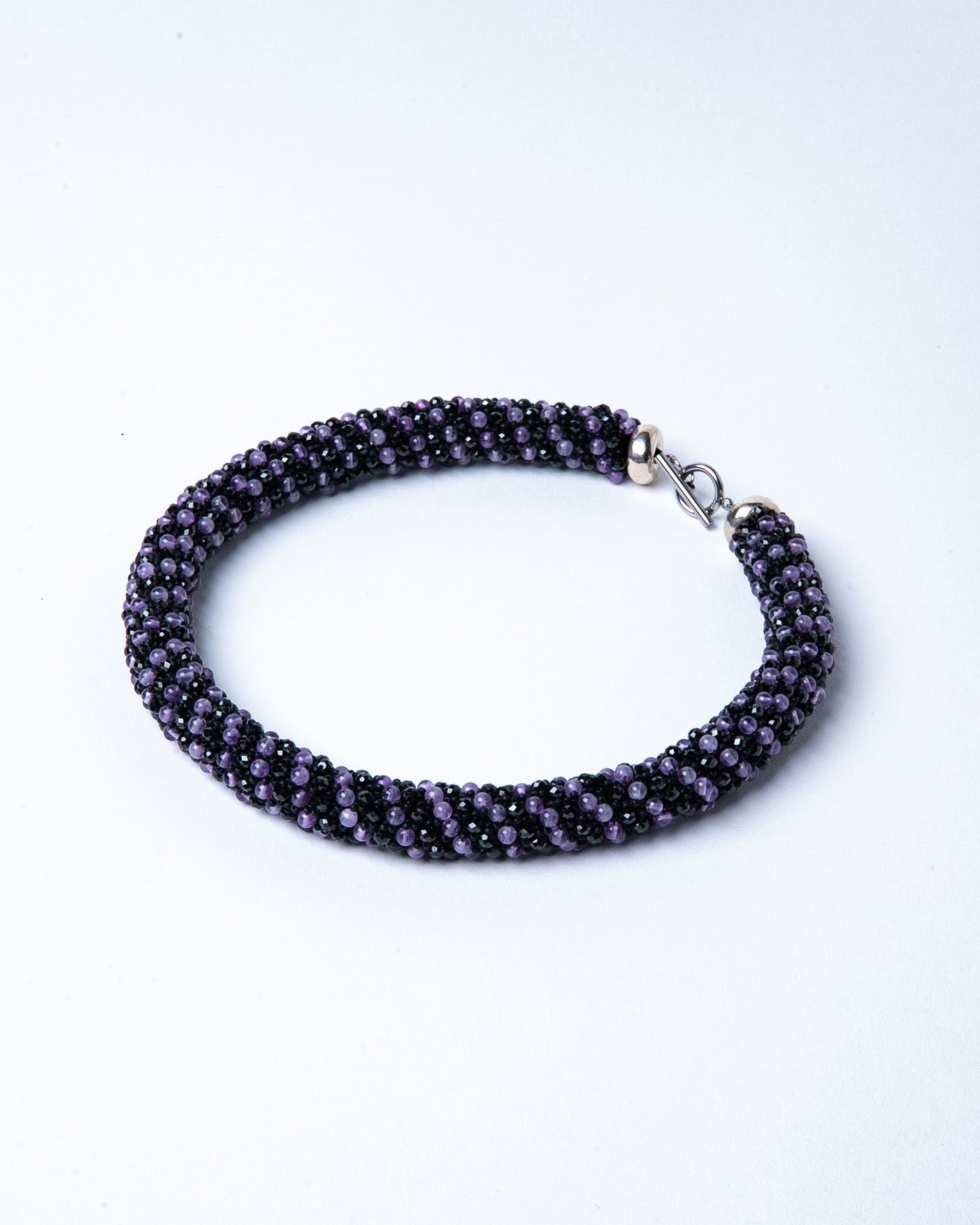 A luxurious amethyst and black spinel necklace with a silver T-bar clasp, featuring vibrant purple and dark sparkling gemstones, crafted in a collar-length design